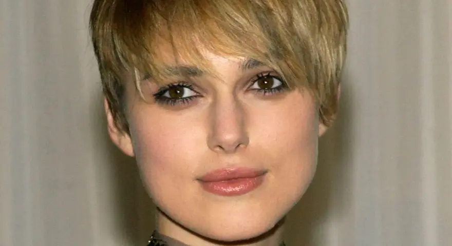 Primo piano di una donna con capelli biondi e tagli corti belli, trucco occhi marcato e un choker decorato.