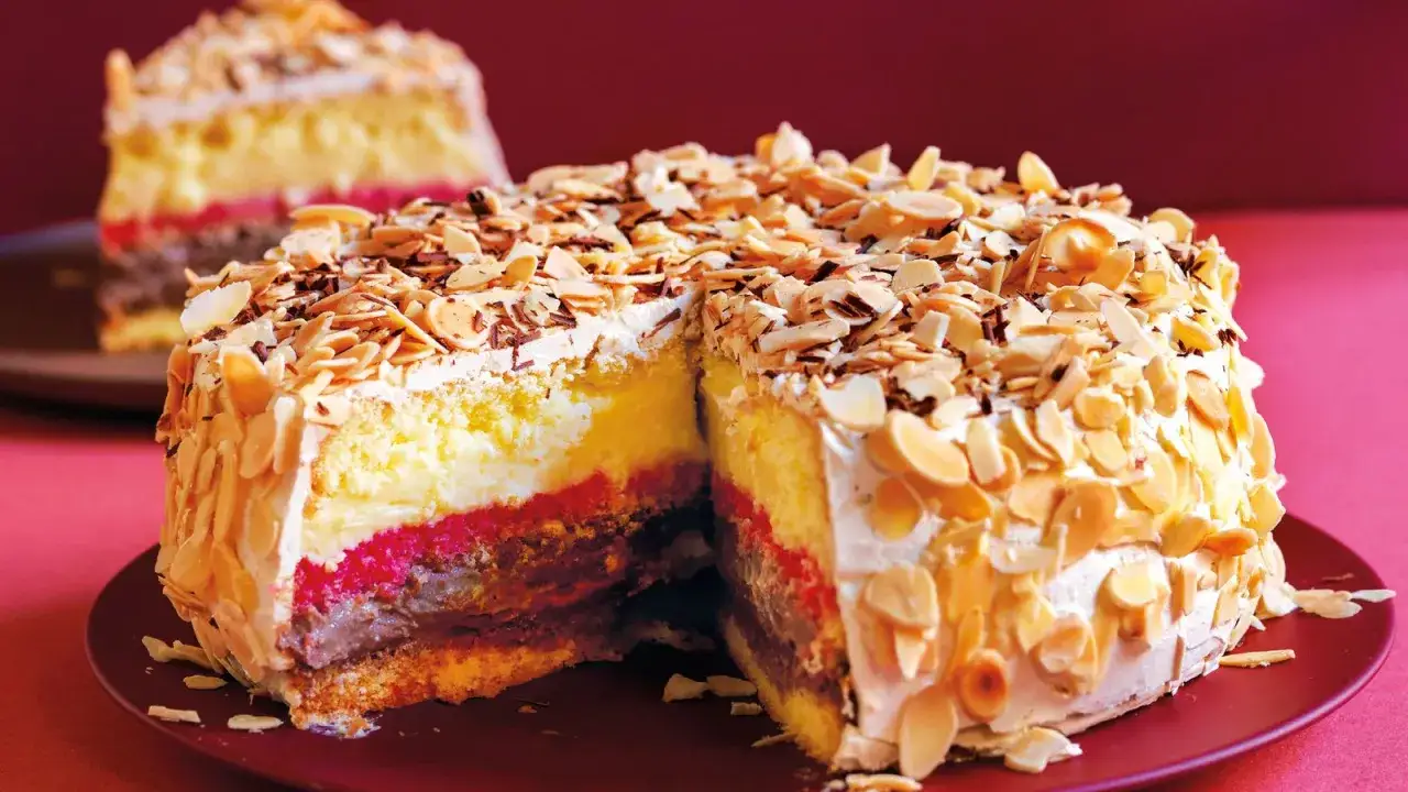 Una fetta di pizza dolce abruzzese, ricoperta di mandorle a lamelle e panna, con strati di crema, marmellata e cioccolato.