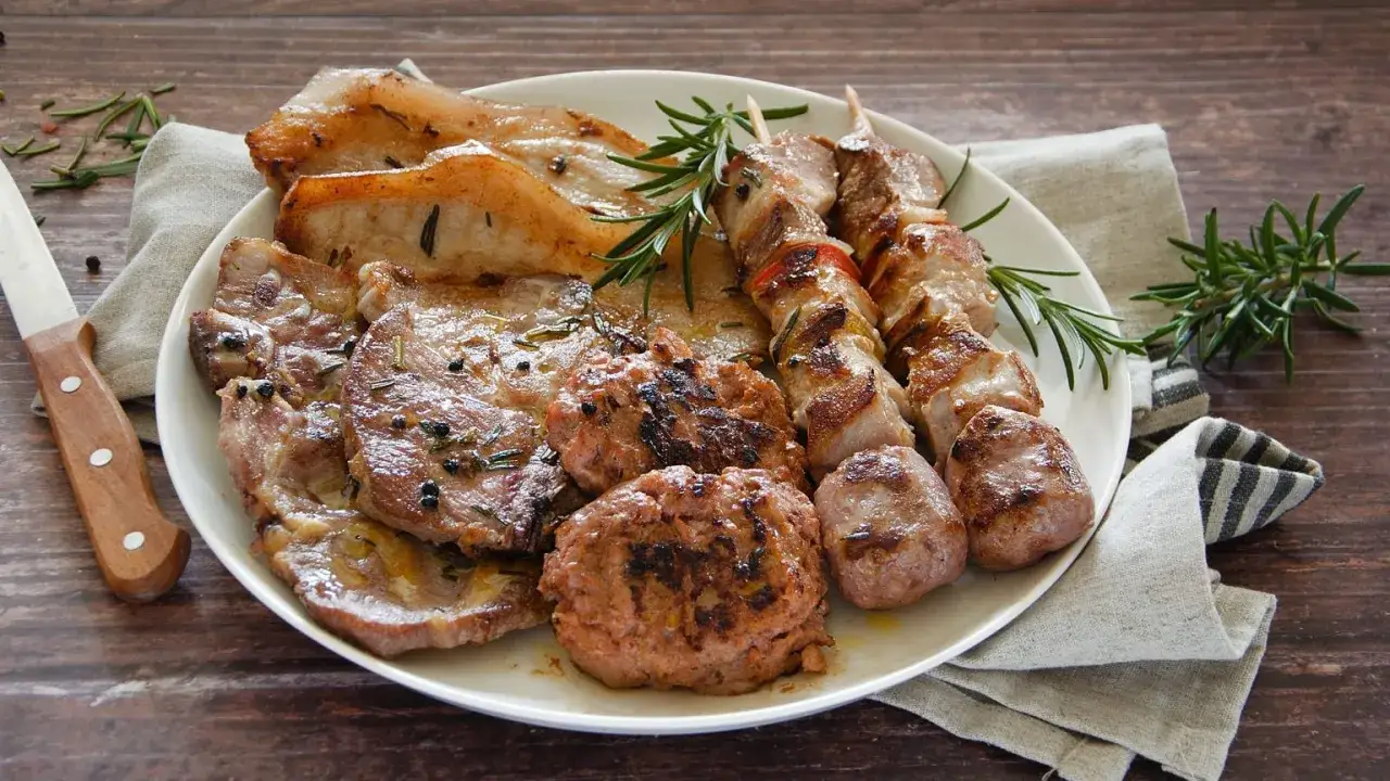 Un piatto invitante con una ricca grigliata di carne: costine, spiedini, salsicce e hamburger, guarniti con rosmarino fresco.