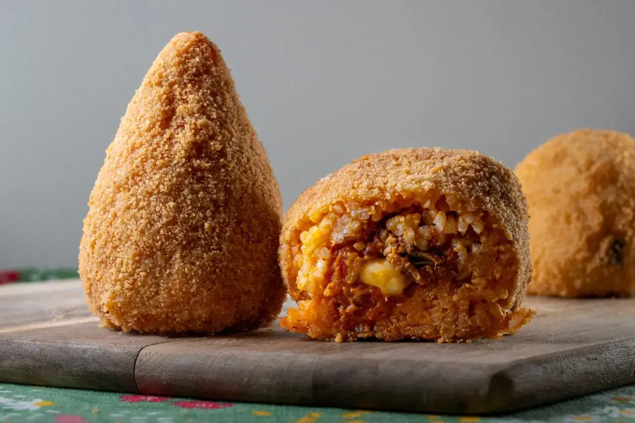 Arancino o arancina dorato e croccante, uno intero a forma di cono, l'altro tagliato a met&agrave; rivelando un ripieno saporito.
