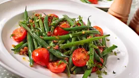 Insalata di fagiolini freschi con pomodorini ciliegino e erbe aromatiche, servita in un piatto bianco.
