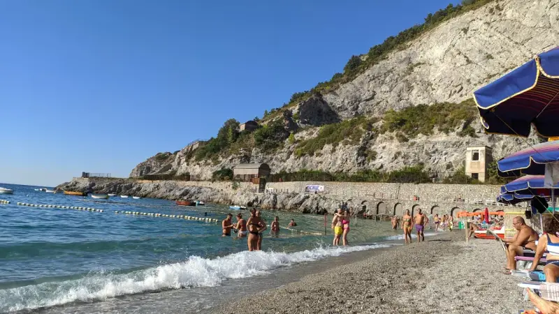 Persone si godono una giornata di sole sulla spiaggia di Erchie, con il mare azzurro e una scogliera imponente alle spalle.