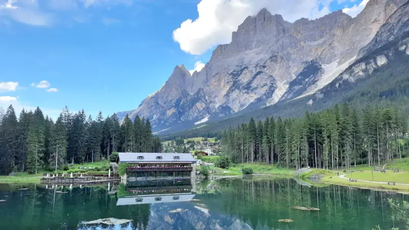 Riflessi alpini sul lago di Mosigo, con un rifugio e montagne imponenti sullo sfondo.